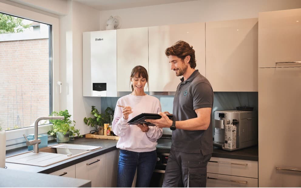 Installateur met klant in de keuken en boiler hangend aan de muur